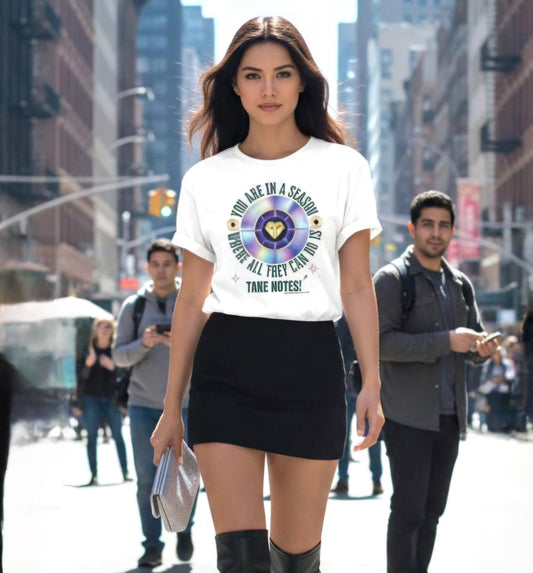 Woman wearing a white t-shirt with a graphic 'You are in a season that all can do is take notes' design on a city street.