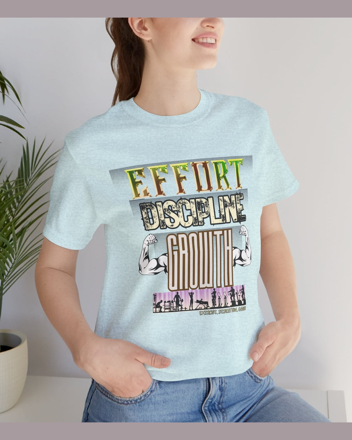 Person wearing a light blue t-shirt with motivational gym text 'Effort Discipline Growth' and flexing arms graphic on a grey background.