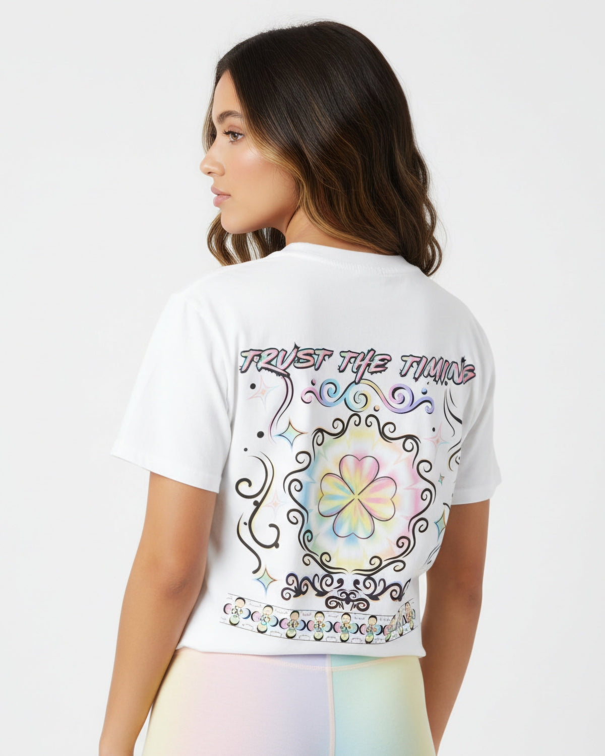 Woman is wearing a white T-shirt with the colorful rainbow clover and a text trust the timing on a white background
