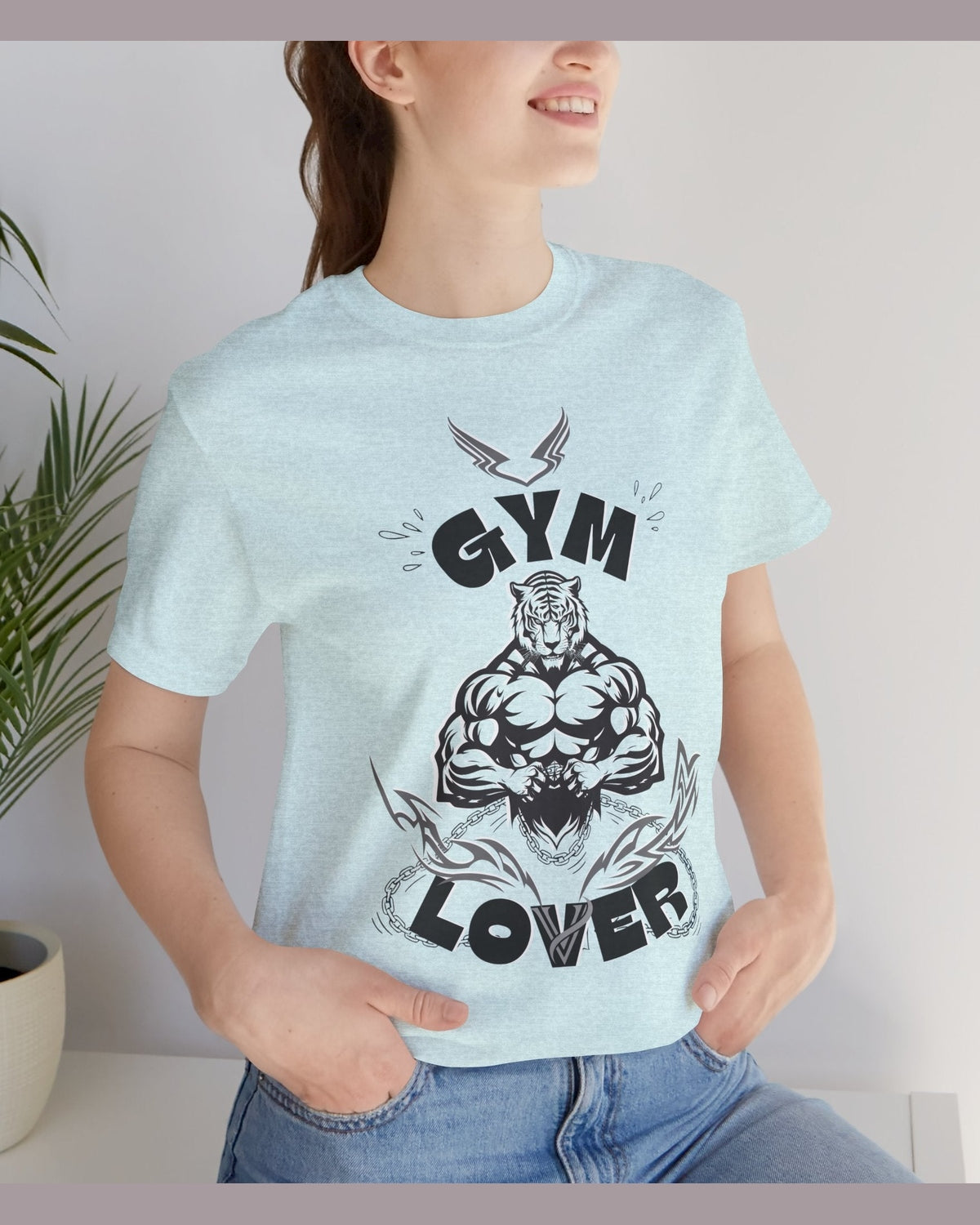 Person wearing a light blue t-shirt with a fitness graphic design and text Gym Lover, standing indoors.