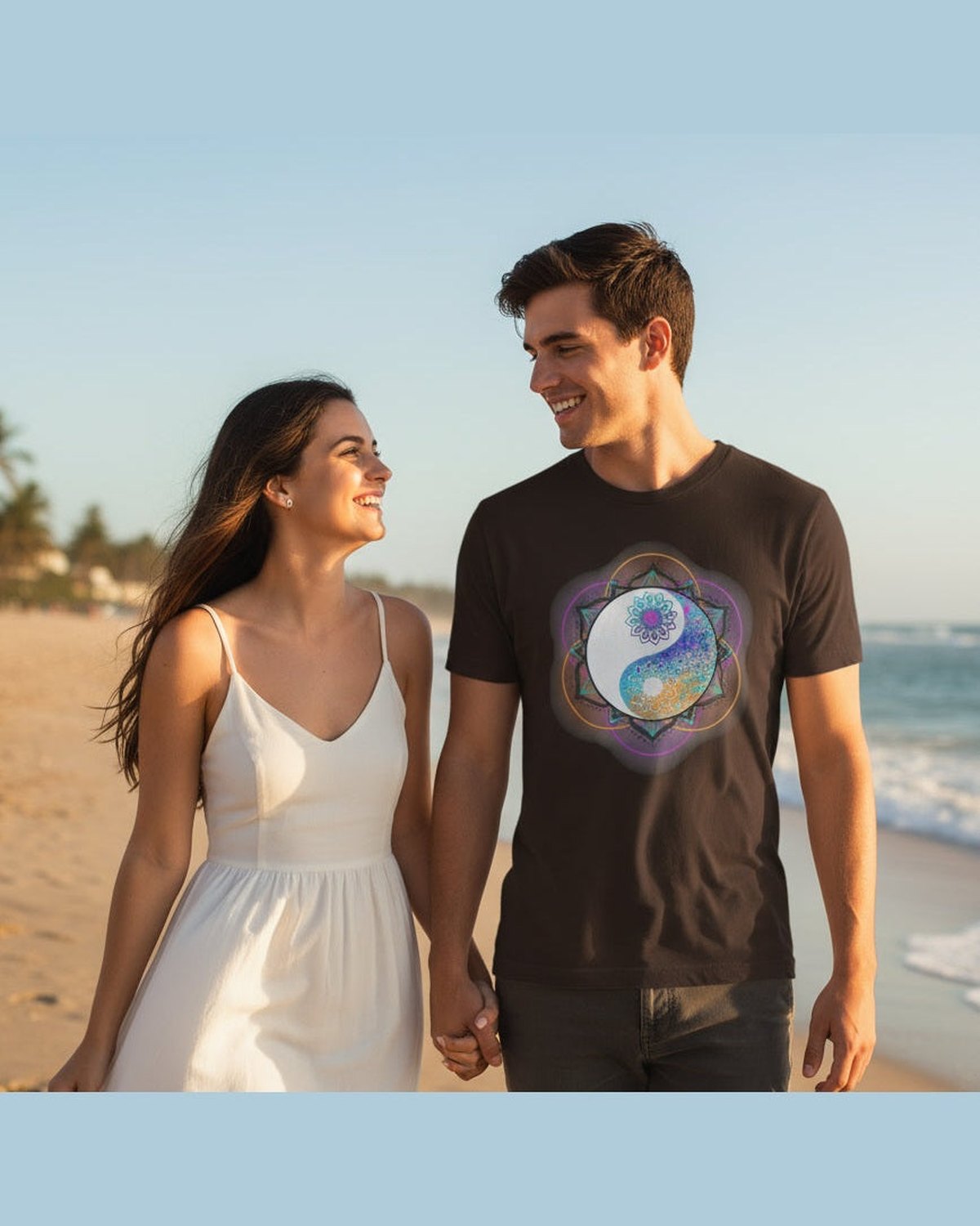 A man wearing a brown t-shirt with a colorful mandala design featuring a yin yang symbol walking on a beach with his girlfriend 