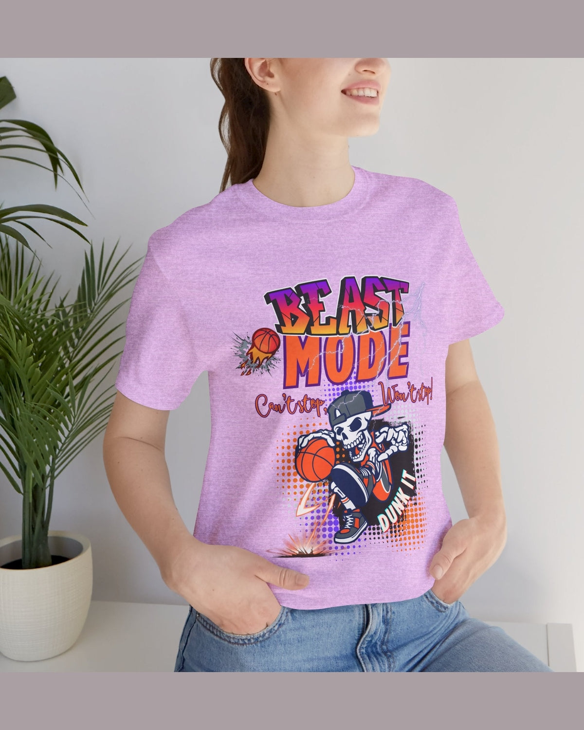 Person wearing a pink t-shirt with a motivational quote 'Beast Mode Cant stop wont stop' and basketball graphic design, standing indoors next to a plant.