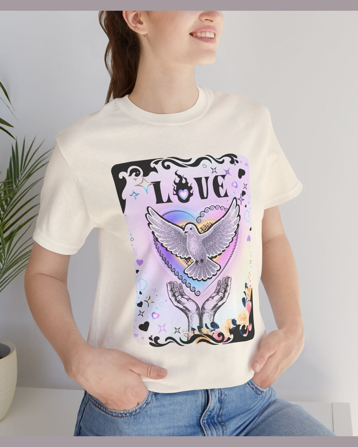Soft yellow tshirt with vibrant pink and purple pastel colours, flowers and a pigeon in rainbow heart coming out of hands with the text Love on a white background 