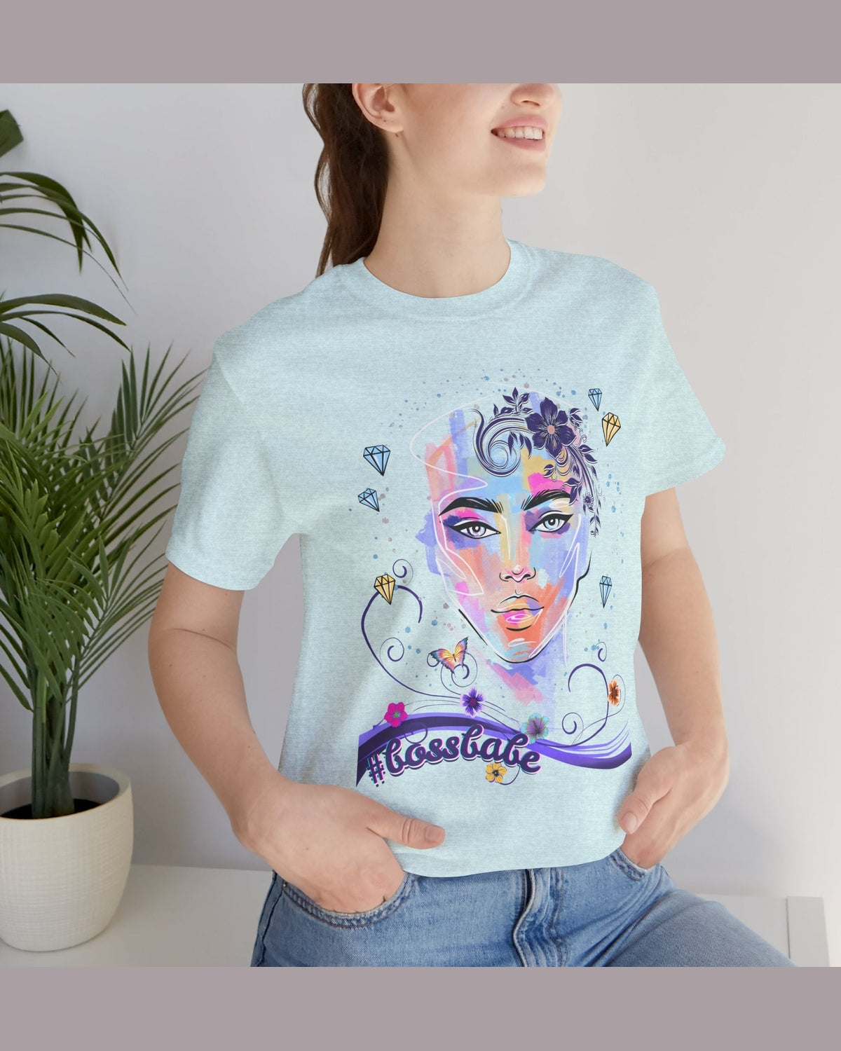 Person wearing a light blue t-shirt with a colorful graphic design of a female face, diamonds and flowers and a text #bossbabe on a white background.