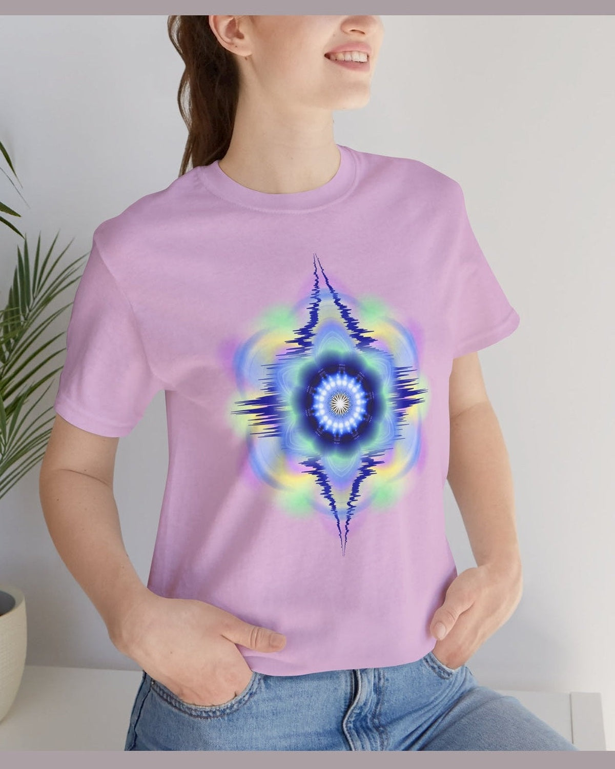 Person wearing a purple t-shirt with vibrant hues abstract design, standing indoors next to a plant.