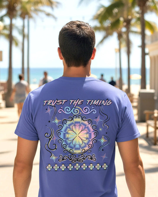 Man wearing a shirt with colourful clover and a text Trust the timing walking on a beach alley