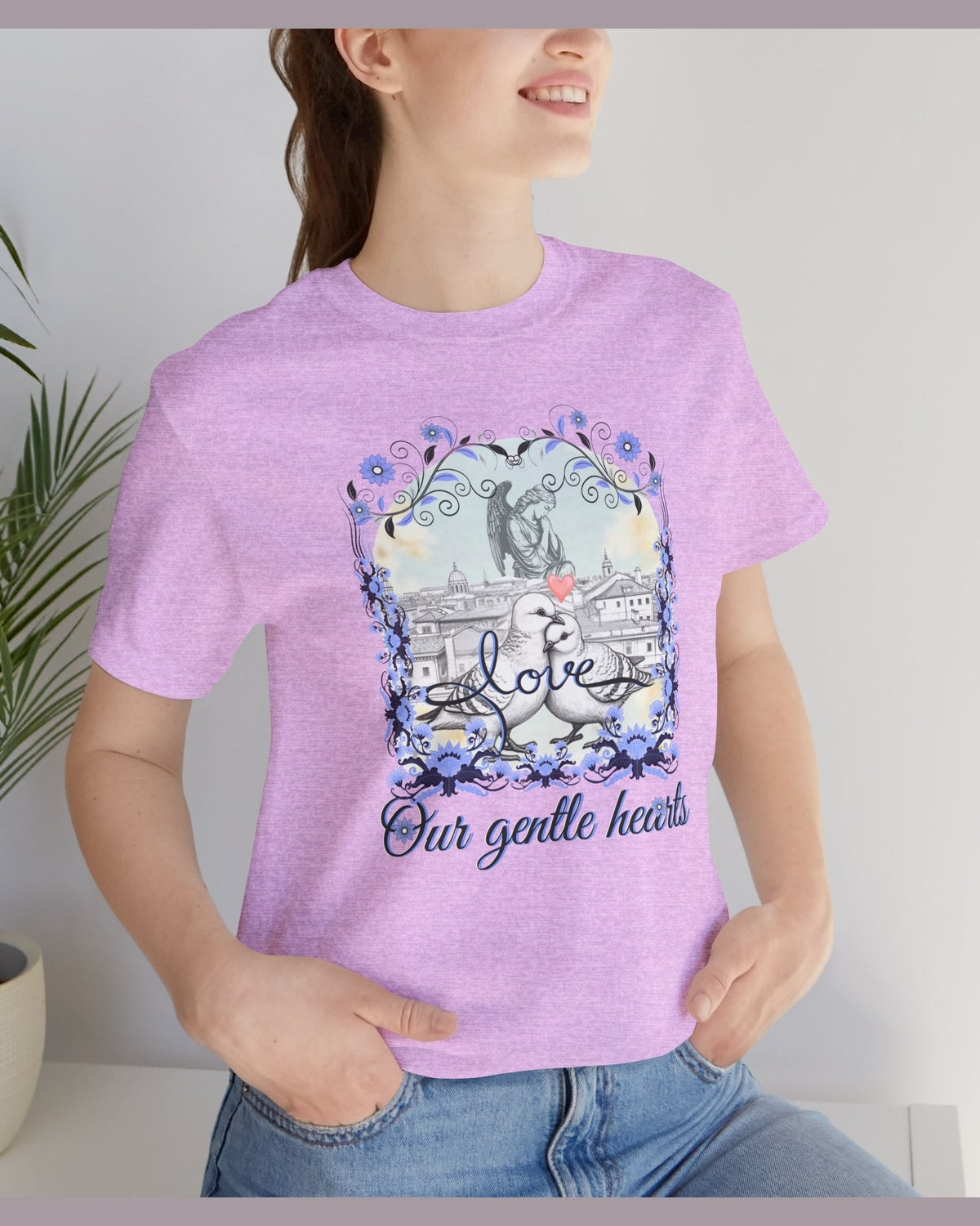 Person wearing a purple t-shirt with a pigeon, angel and floral graphic design and text.