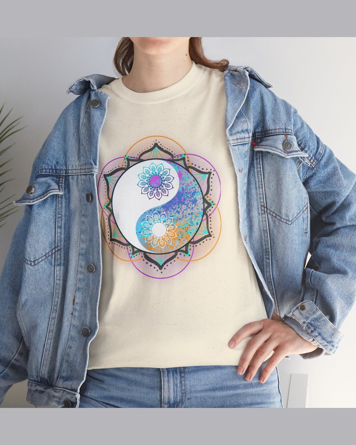 Person wearing a cream t-shirt with a colorful floral yin yang mandala design, paired with a denim jacket.