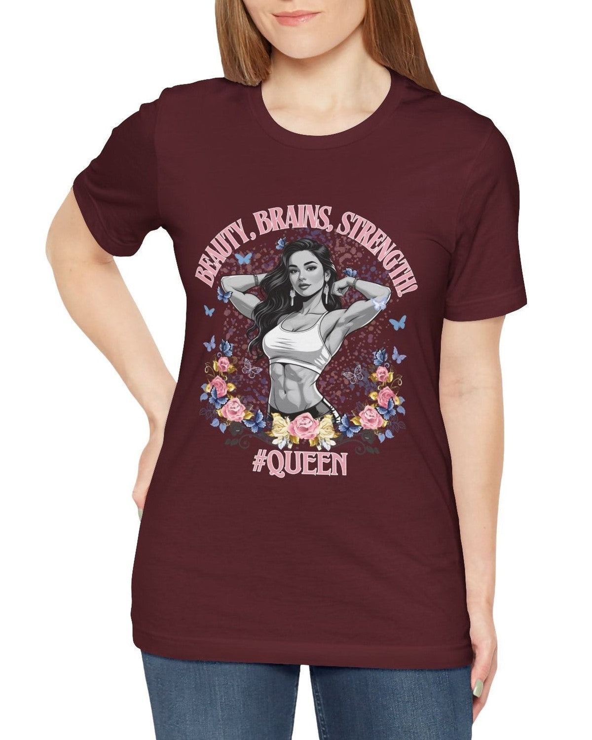 Woman wearing a maroon t-shirt with a graphic design of a fitness woman, flowers, butterflies and text 'Beauty, Brains, Strength #Queen' on a white background