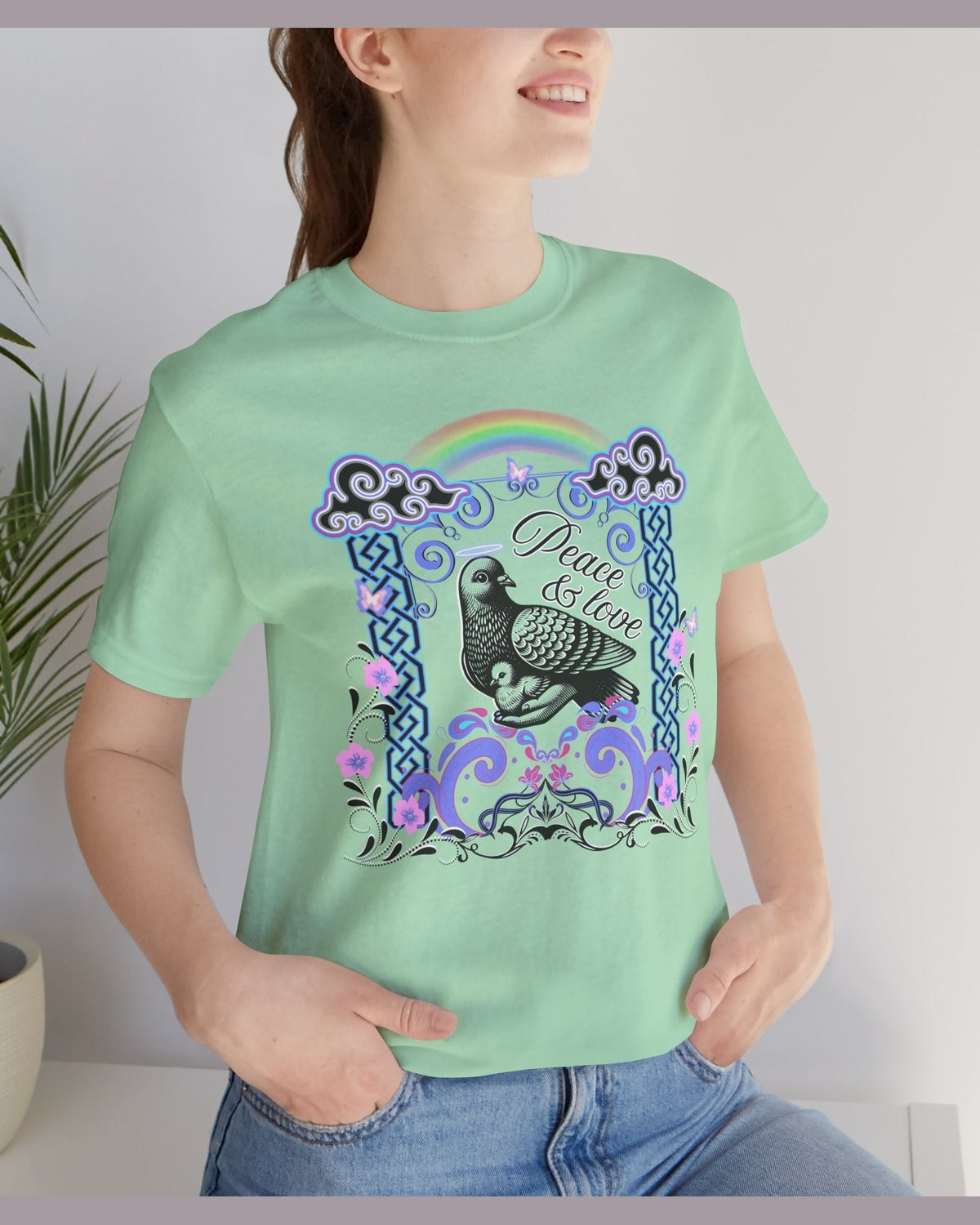 Person wearing a light green t-shirt with a colorful design featuring a dove, rainbow, and text Peace & Love.