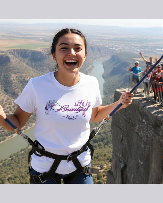 Person on a cliffside adventure wearing a 'Life is Beautiful' t-shirt with scenic background.