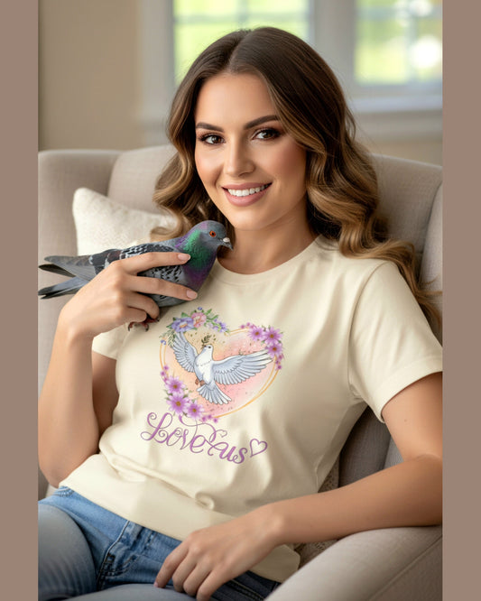 Woman wearing a soft yellow t-shirt with a dove and floral heart design, sitting on a couch holding a bird.