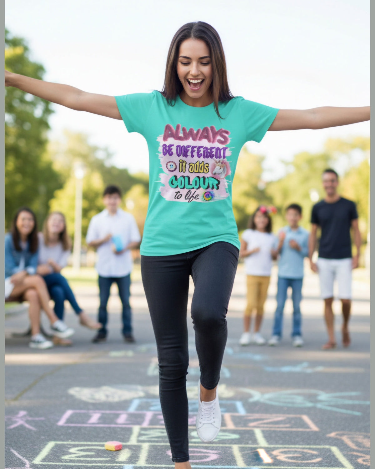 Woman wearing a green t-shirt with a colorful inspirational message Always Be Different, standing outdoors with people in the background.