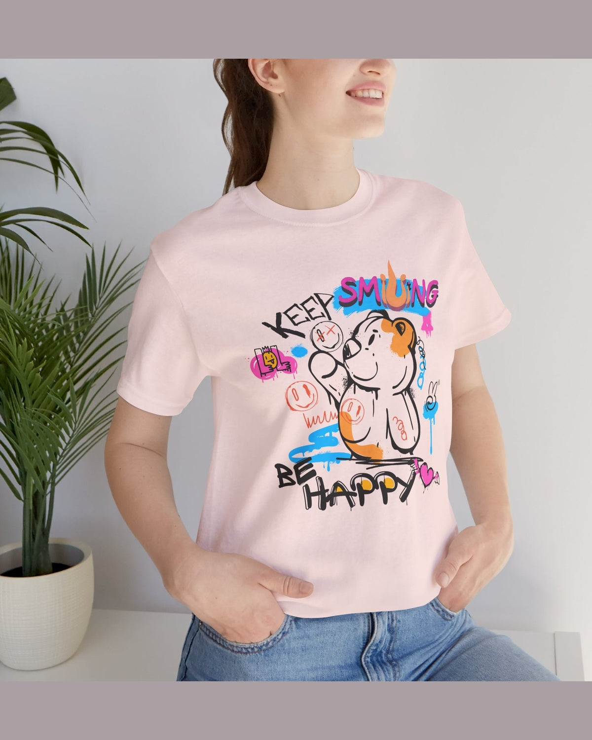 Person wearing a pink t-shirt with colorful graphics and text Keep Smiling Be happy