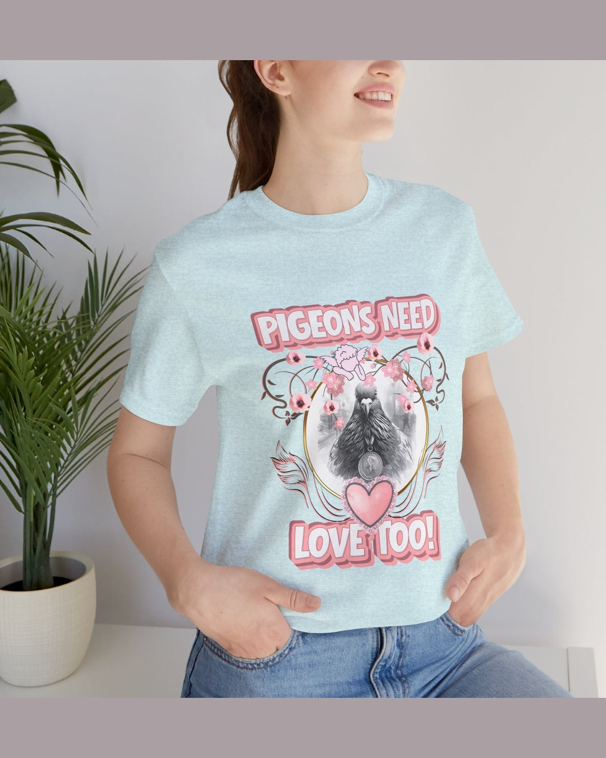Person wearing a light blue t-shirt with a pigeon graphic and text Pigeons need love too, standing indoors.