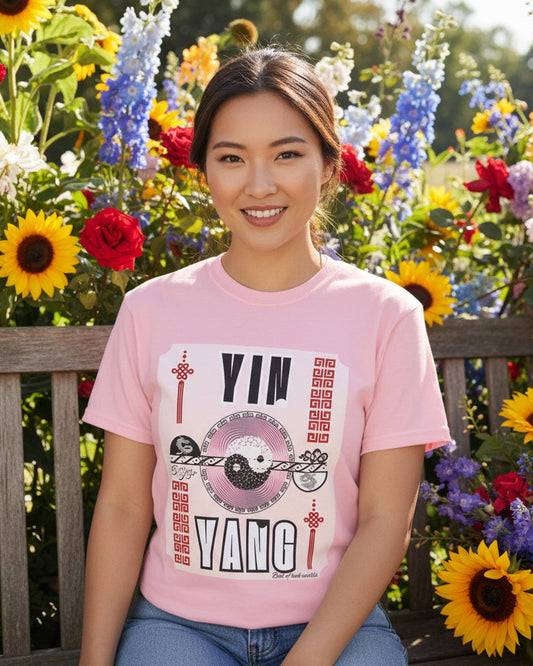 Person wearing a pink t-shirt with 'Yin Yang' design, sitting on a bench near flowers