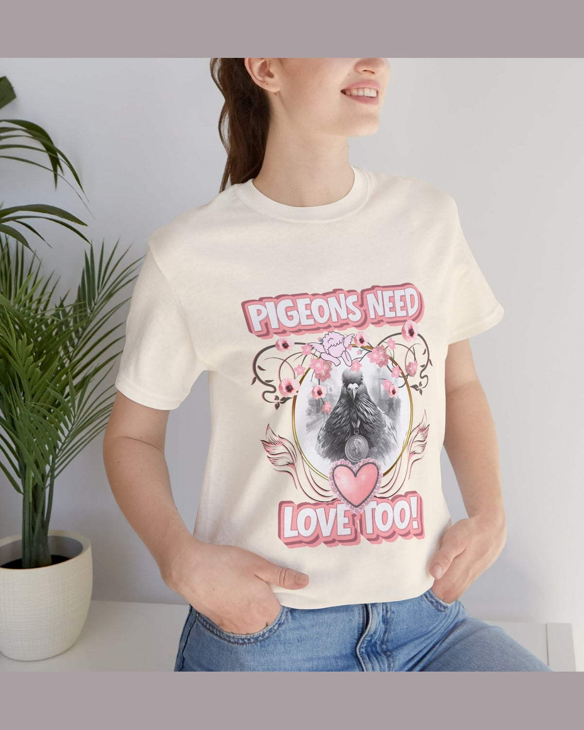 Person wearing soft yellow t-shirt with a graphic design of a pigeon and text 'Pigeons Need Love Too!' in a home setting.