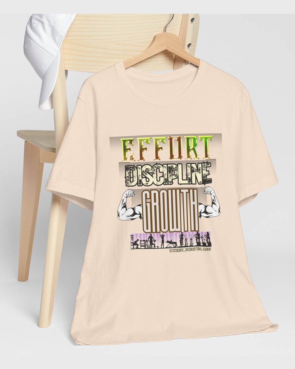 Beige t-shirt with motivational gym text 'Effort Discipline Growth' and flexing arms graphic on a wooden chair against a white background