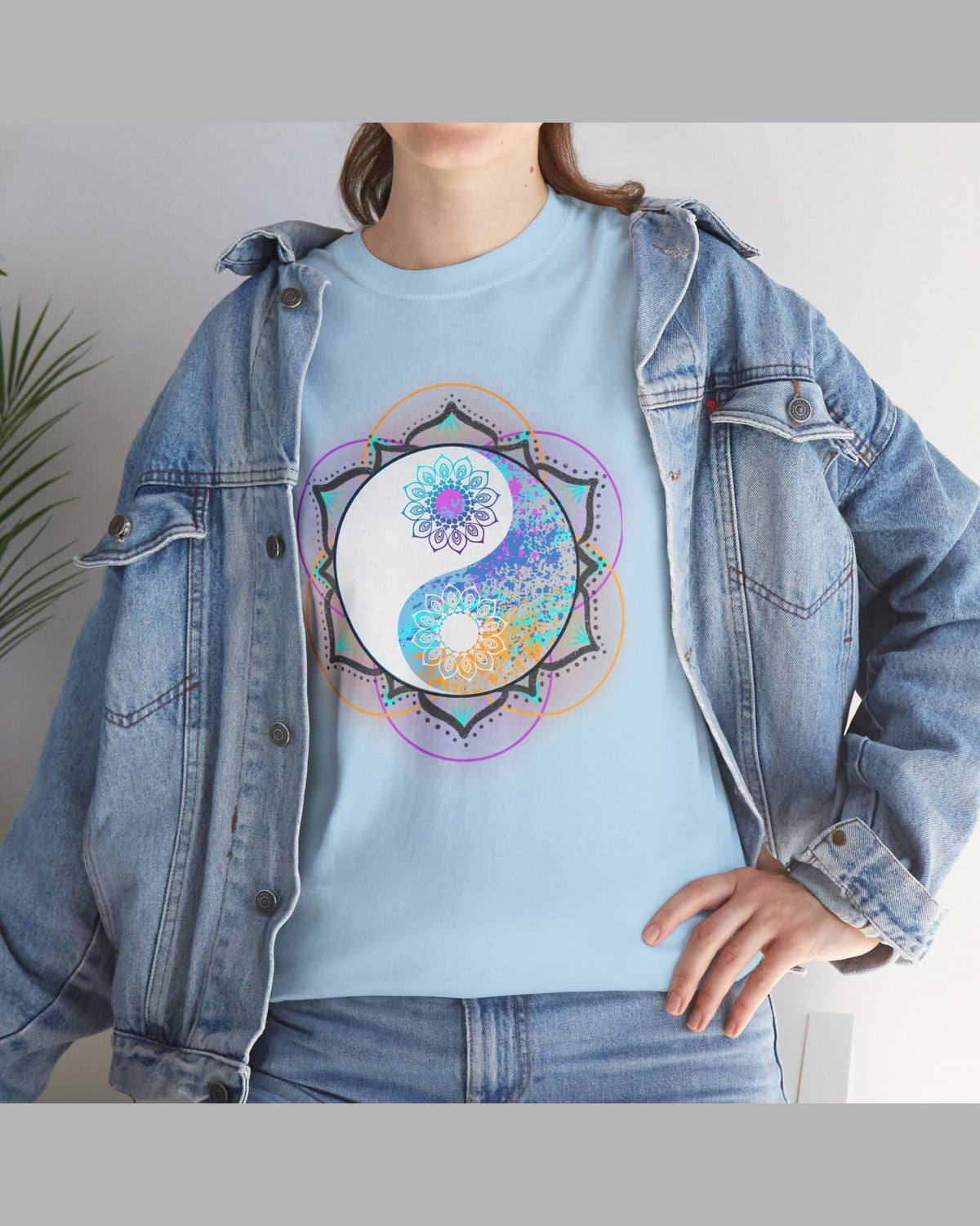 Person wearing a light blue t-shirt with a colorful floral yin yang mandala design, paired with a denim jacket.