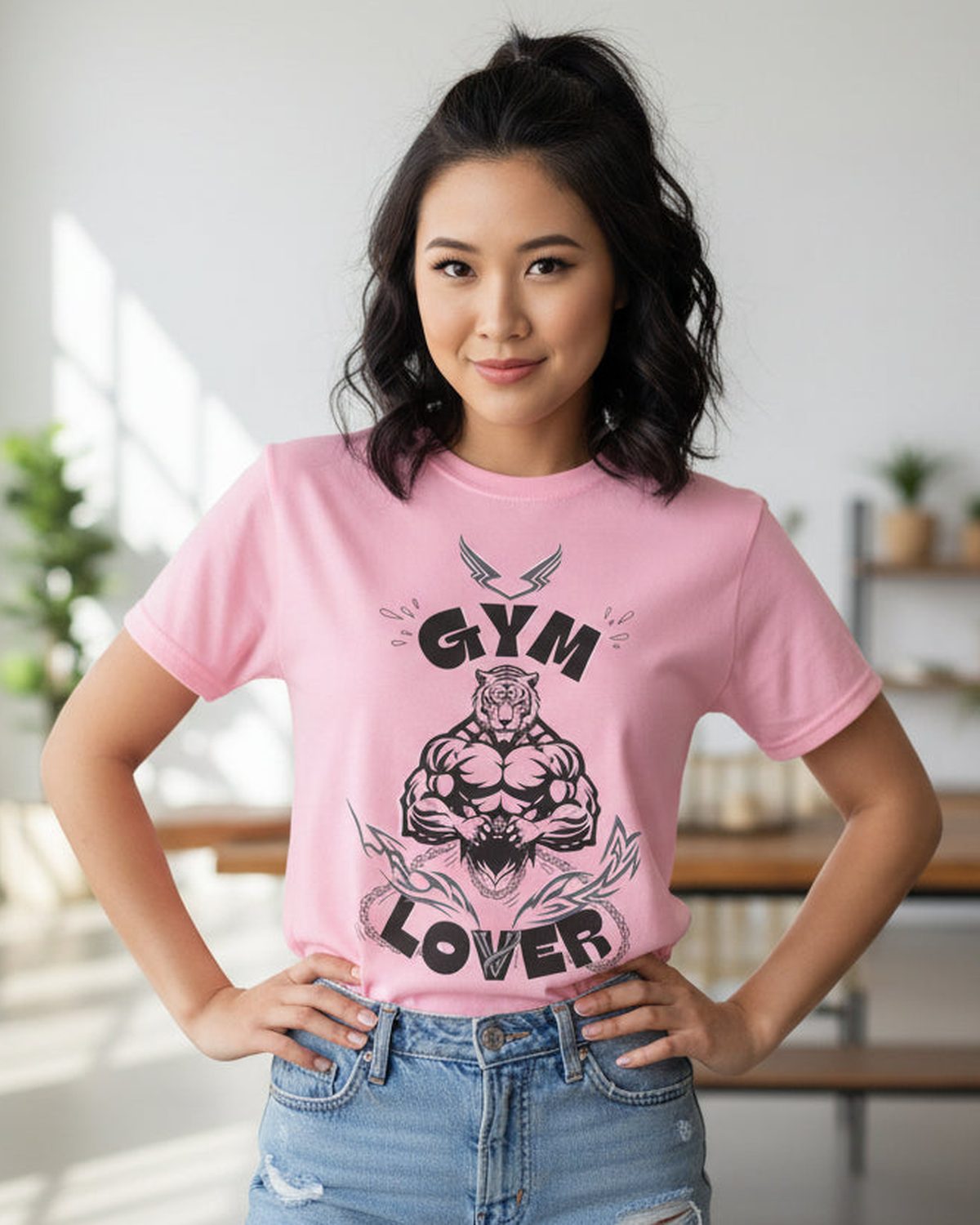 Woman wearing a pink tshirt with black graphic design featuring a muscular tiger and 'Gym Lover' text in a bright room.