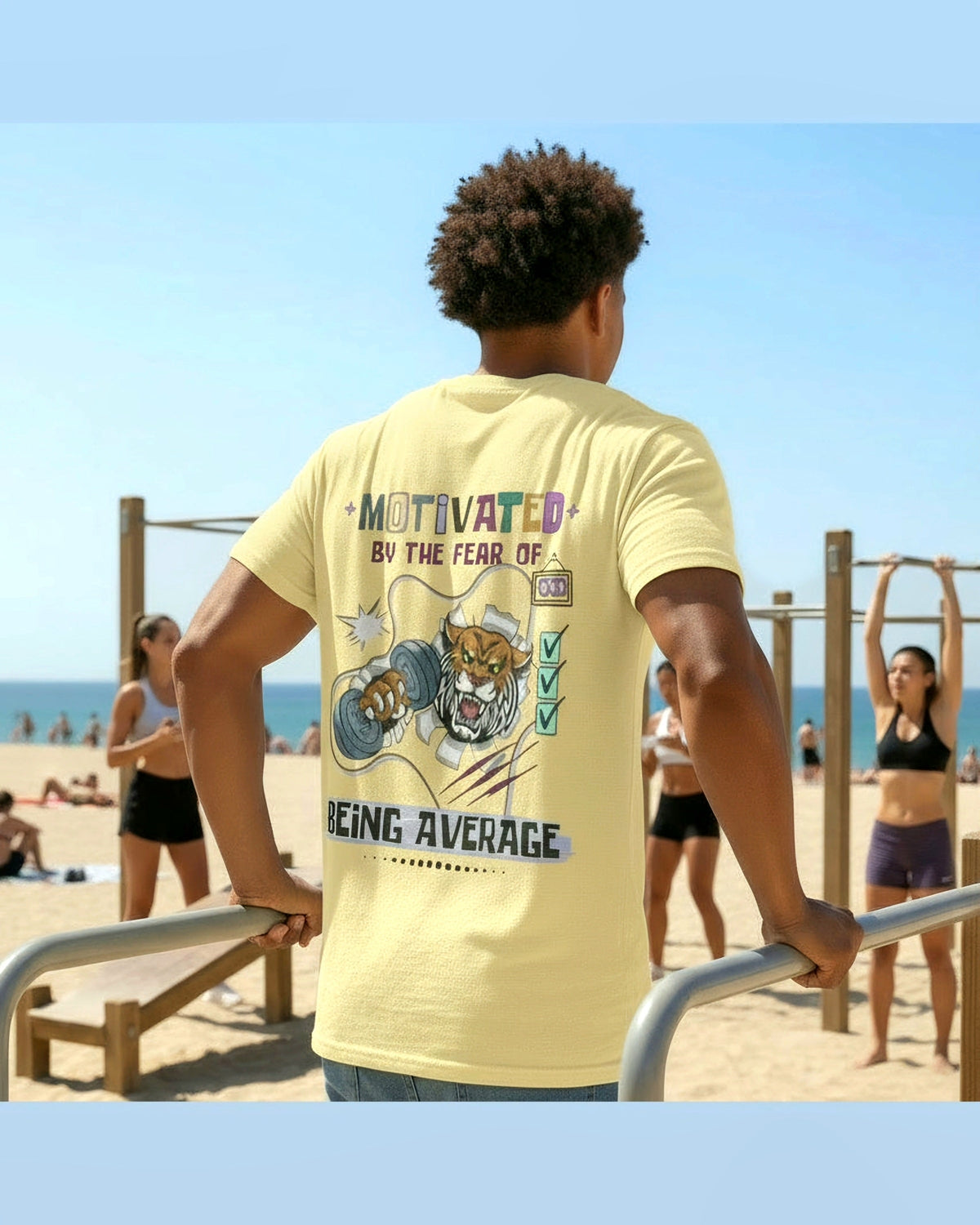 Person wearing a yellow t-shirt with motivational fitness design and text 'Motivated by the fear of being average' doing dips at a beach fitness