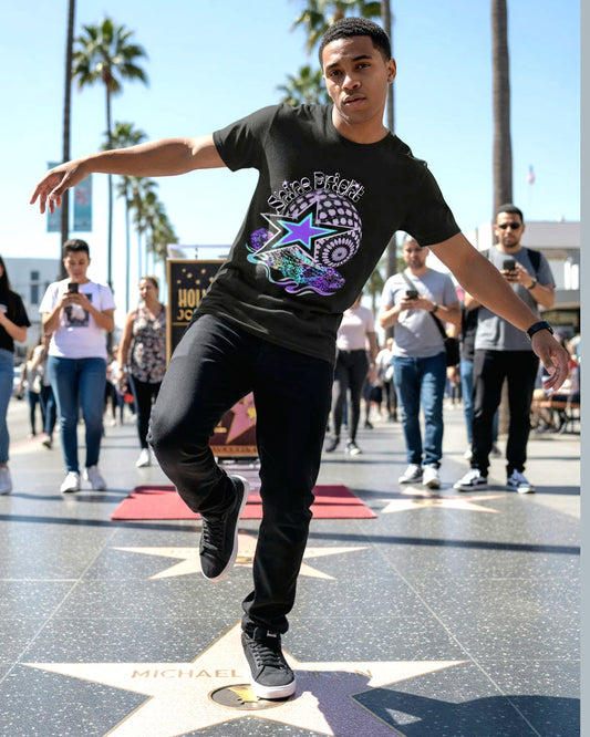 Man wearing a Black empowering t-shirt with a colorful star and globe design and text Shine Bright stepping on a star in the pavement of a lively centre