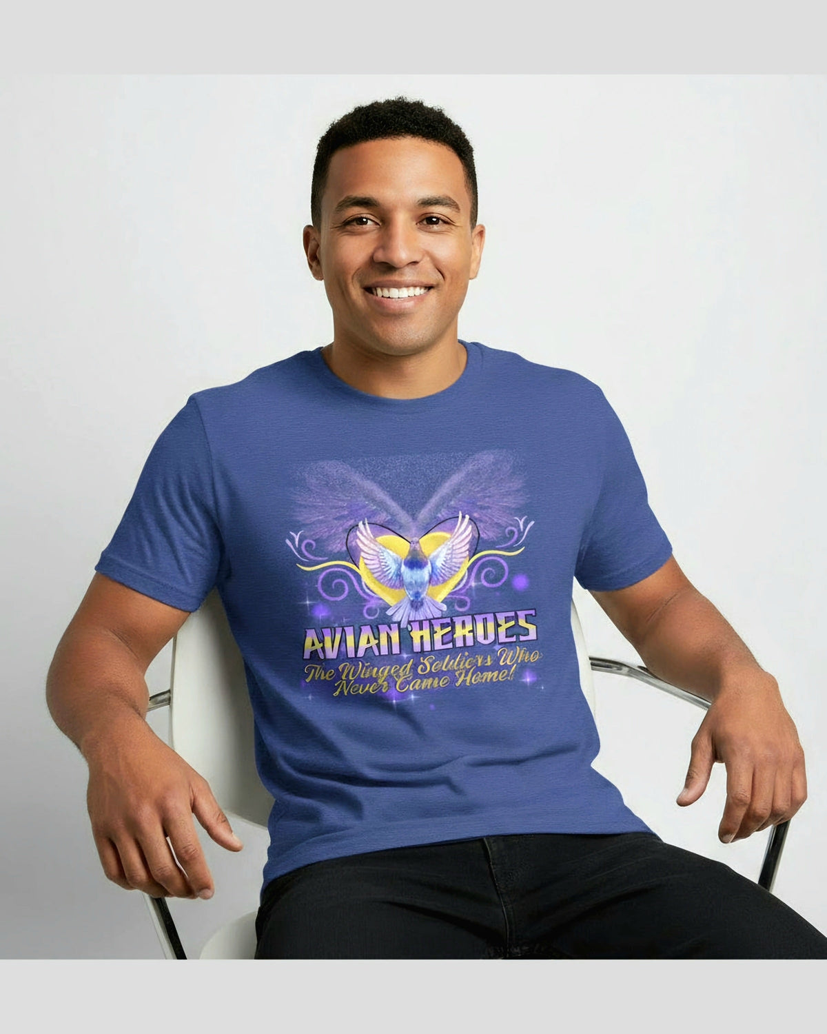 Man wearing a blue t-shirt with a pigeon graphic design and text Avian Heroes, sitting on a white chair against a light gray background.