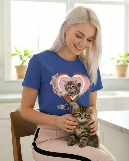 Woman wearing a blue t-shirt with a cat design, holding a kitten in a kitchen.
