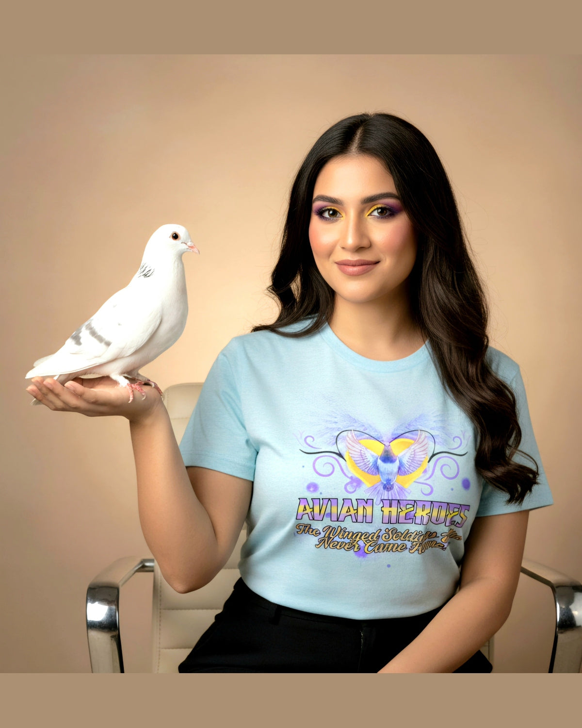 Woman wearing a light blue t-shirt with a pigeon design and text Avian heroes, holding a white dove against a beige background.