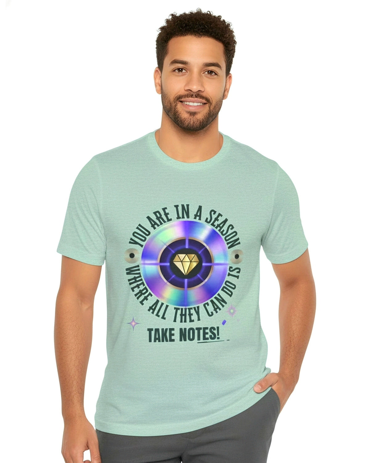 Man wearing a light green t-shirt with a graphic design and text You are in a season where all they can do is take notes on a white background