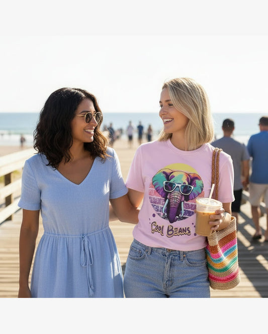 Woman wearing a pink t-shirt with a colorful elephant graphic and 'Cool Beans' text near the sea