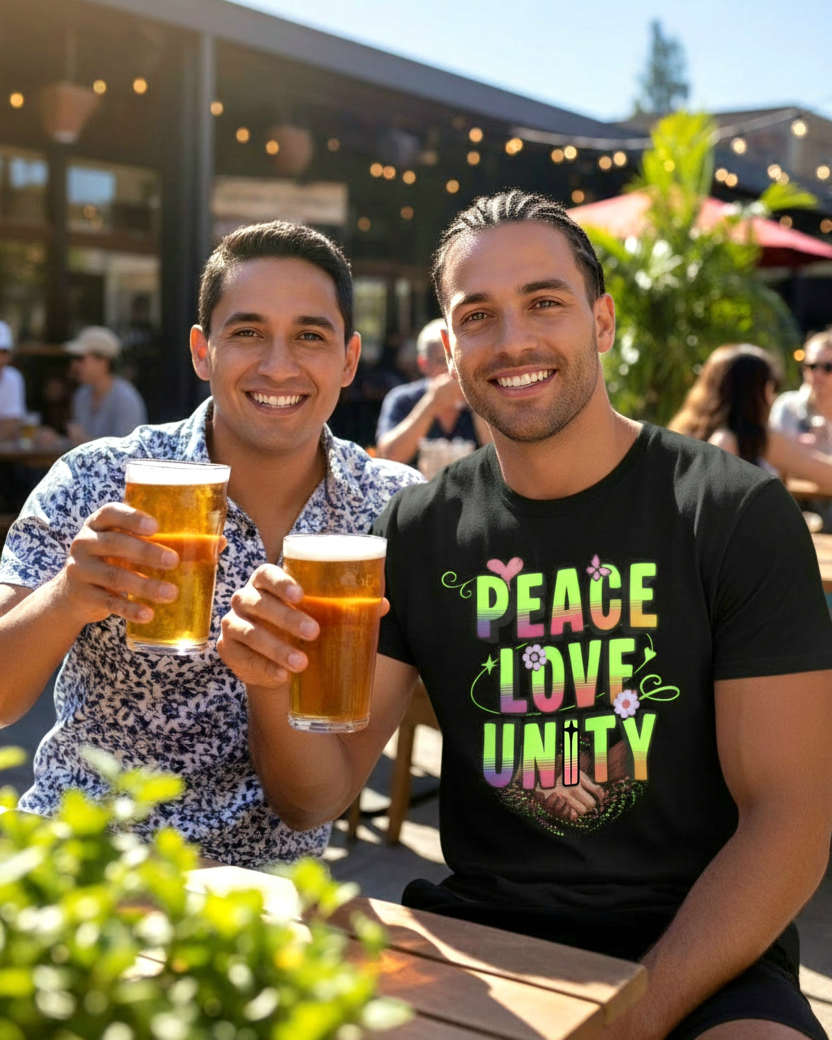 Two men enjoying drinks outdoors, one wearing a 'Peace Love Unity' shirt.